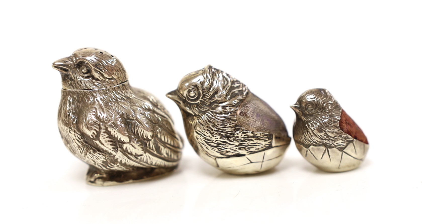 Two Edwardian silver mounted novelty pin cushions, modelled as hatching chicks, by Sampson Mordan & Co, Chester, 1906 & 1908, tallest 27mm, together with a similar novelty chick pepperette, same maker, Sheffield, 1906.